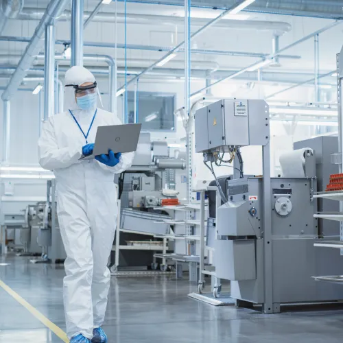 Life Sciences worker in protective gear using a tablet in a modern, bright factory setting.