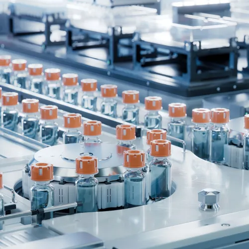 Vials with orange caps on a conveyor belt in a sterile manufacturing lab.